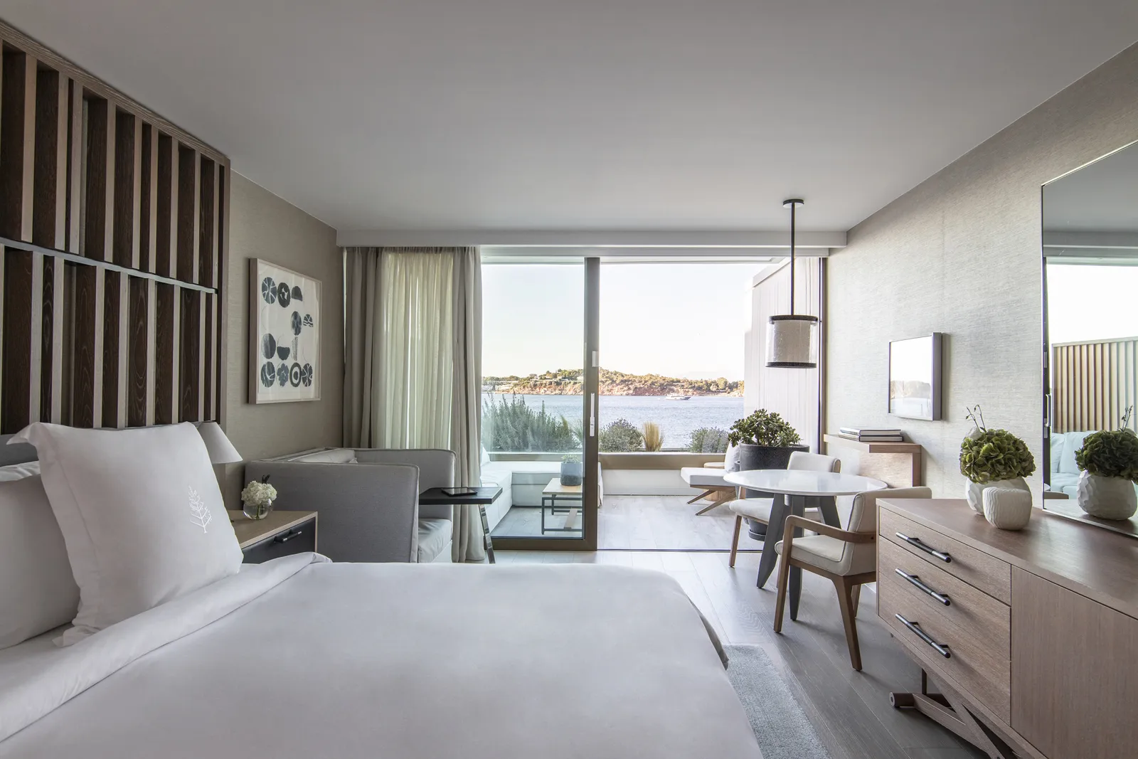 A Nafsika room, with the bed facing the window wall, a slatted timber screen, a round table and the terrace over the sea.