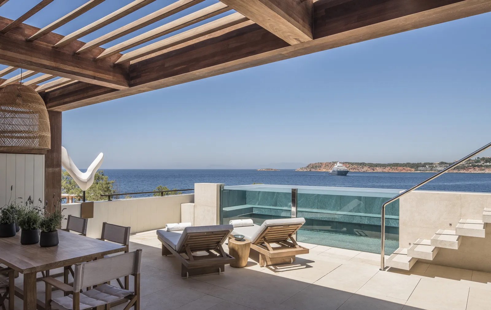 The terrace of a Nafsika Terrace Suite: a timber pergola, a table, 2 loungers and the glass-walled plunge pool over the sea.