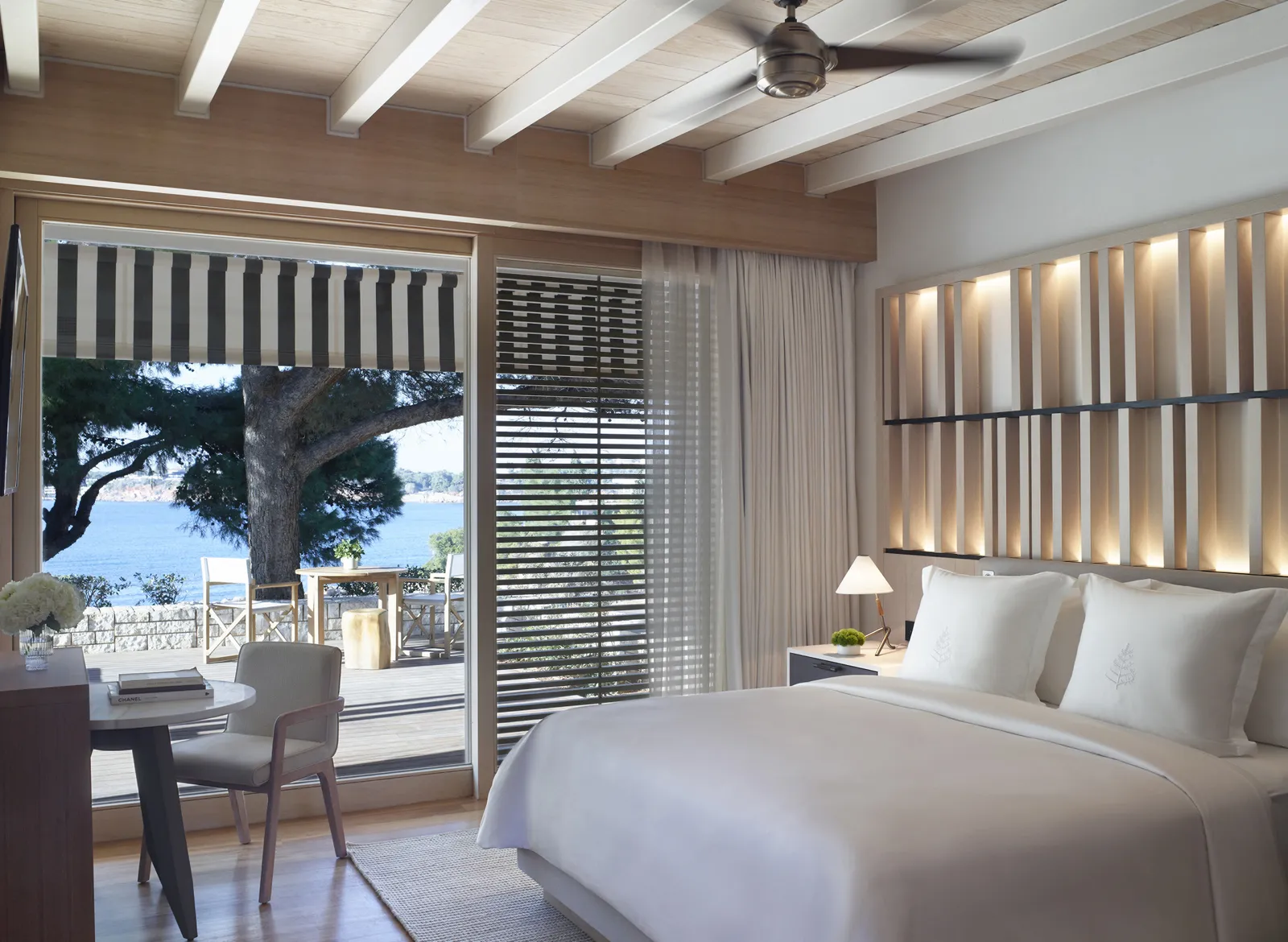 A sea-view bungalow, with a white beamed ceiling, the bed, a desk and the door open to the terrace and the bay through the pines.