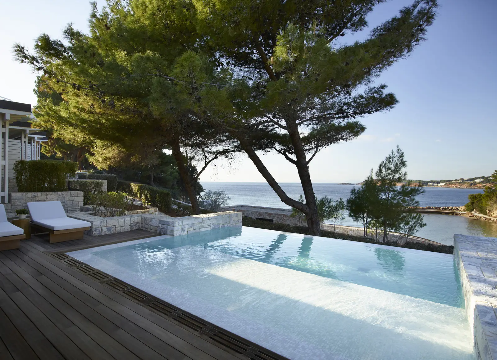 A bungalow’s private pool, set into the timber deck under a large pine, with loungers and the sea a few metres away.