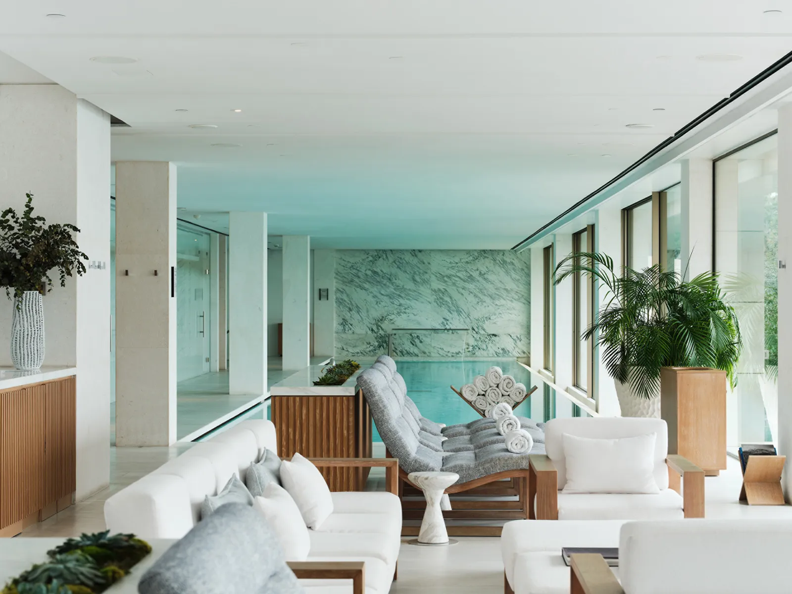 The spa’s lounge, with white armchairs and reclining chairs in front of the indoor pool lined in green marble.