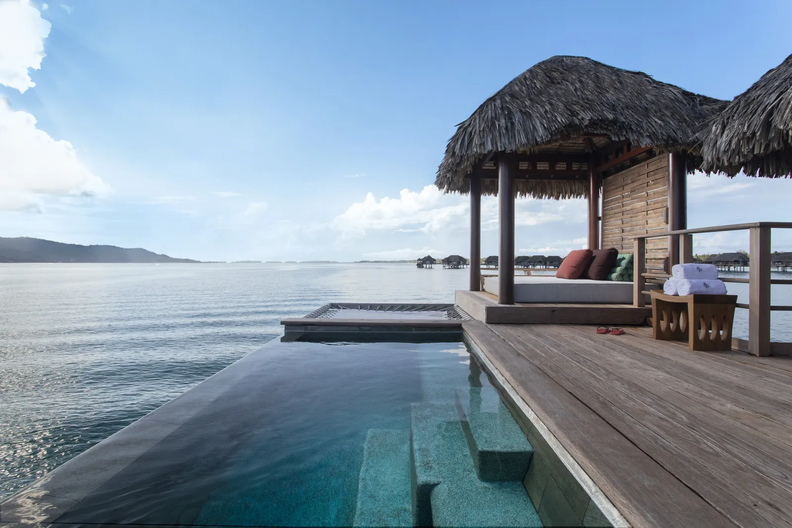 An infinity plunge pool on the deck beneath a thatched pavilion, facing the lagoon