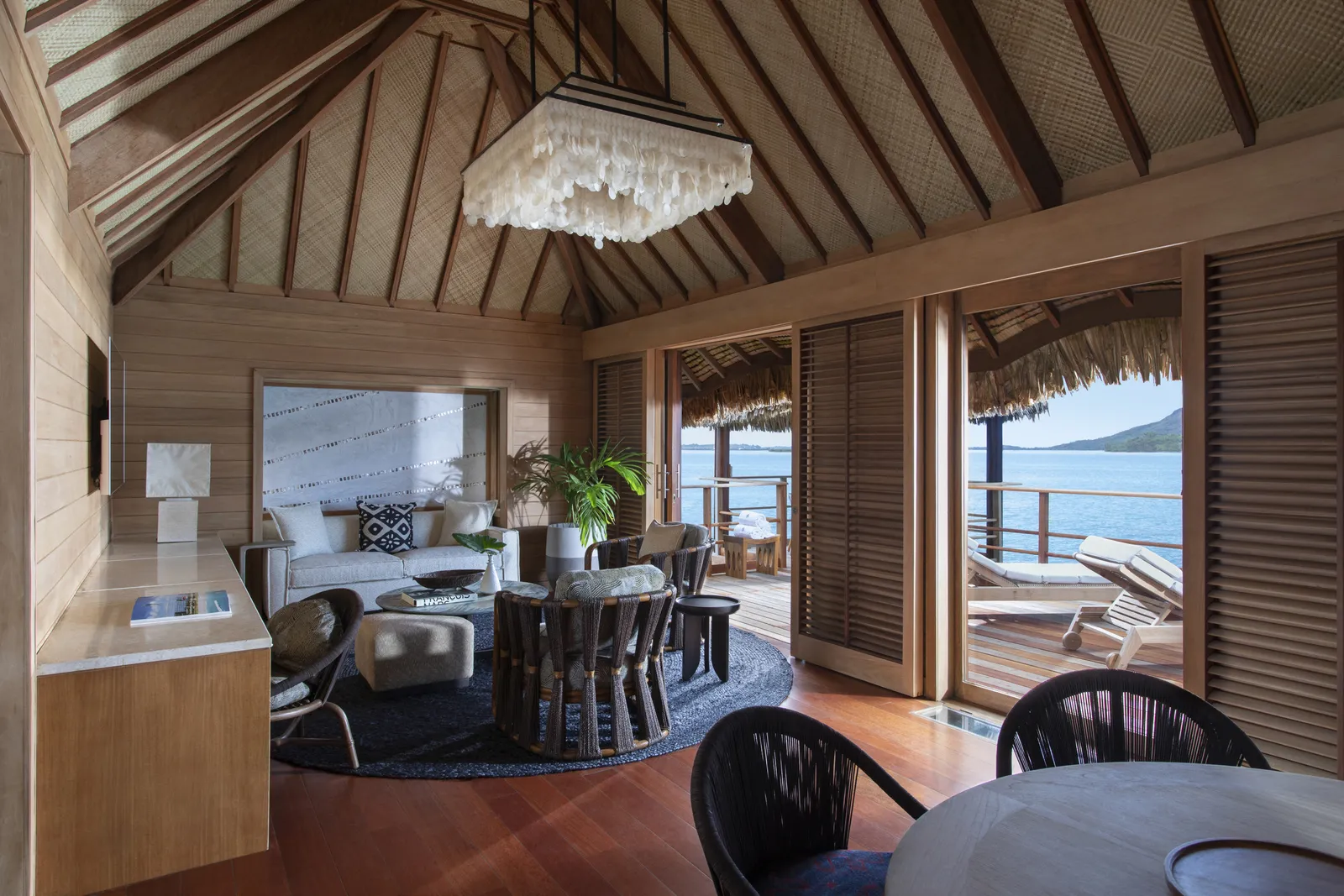 The sitting and dining room under a thatched ceiling with a shell chandelier
