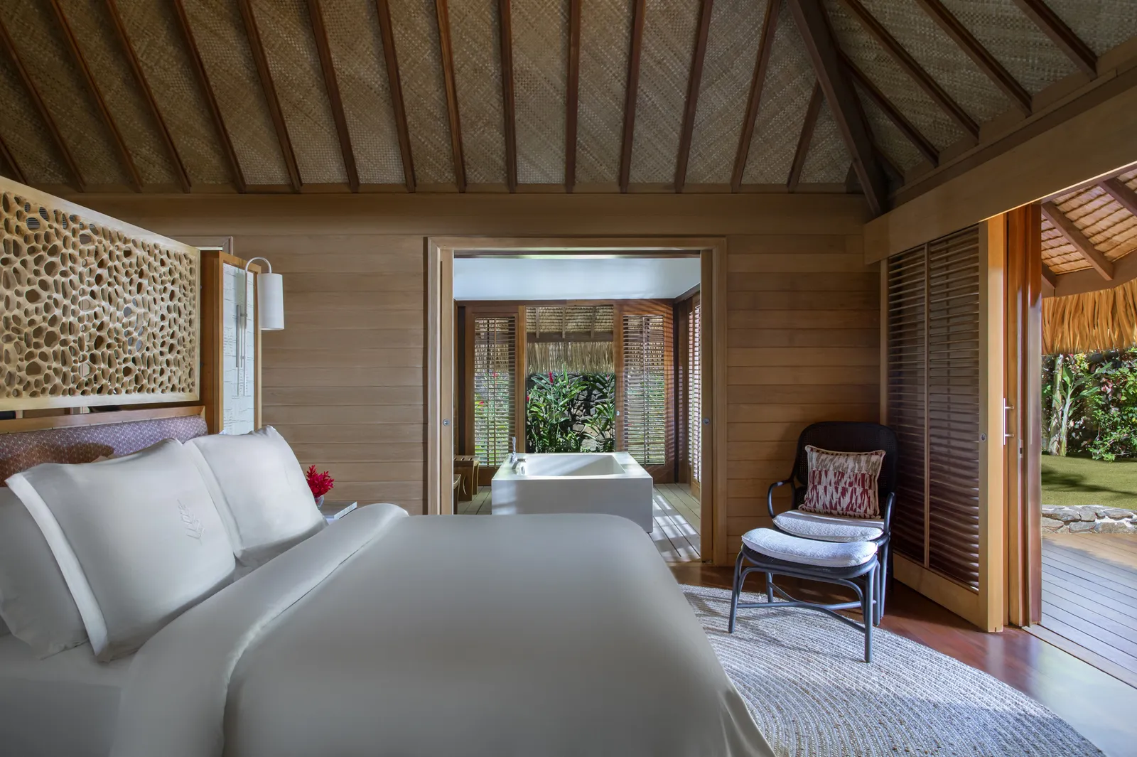 A villa bedroom: a white bed, a tub and the garden beyond the door