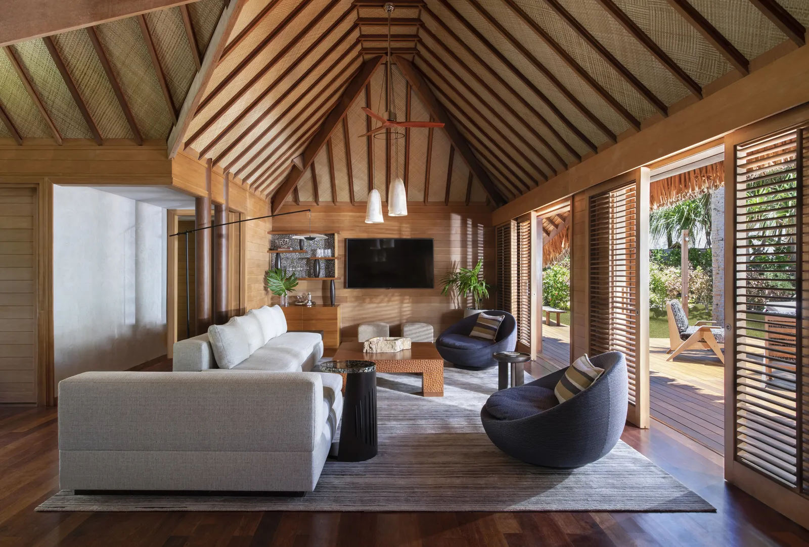 A villa sitting room, white sofas under a timber ceiling, open to the garden