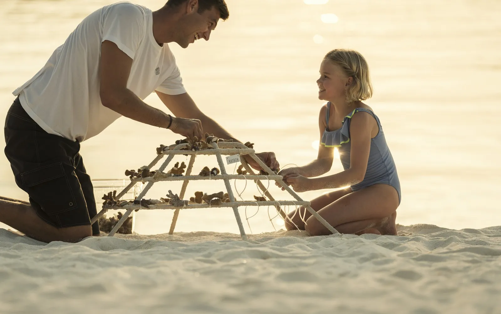 A father and daughter fixing coral fragments onto a frame on the beach