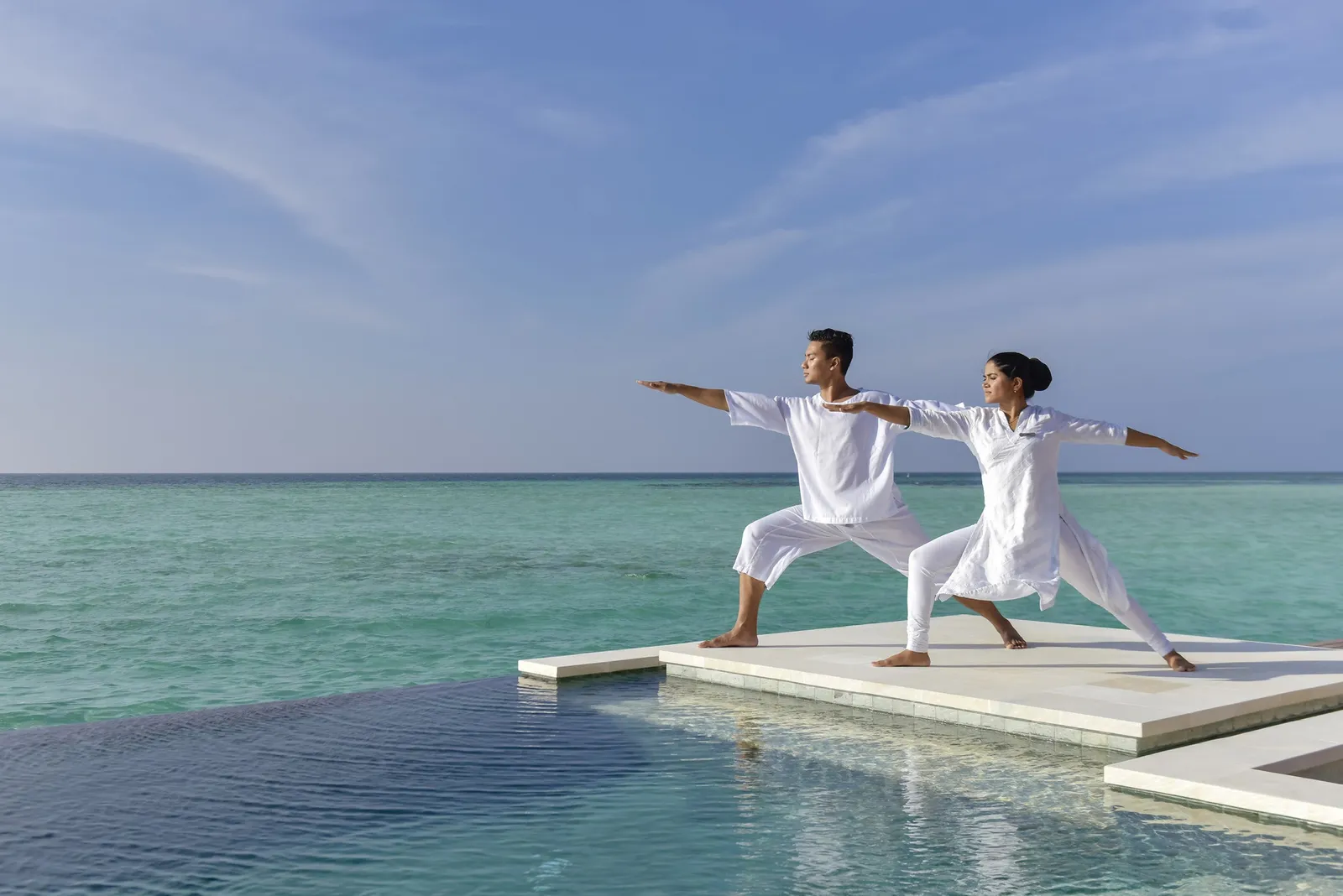 2 people doing yoga on a white platform over the sea