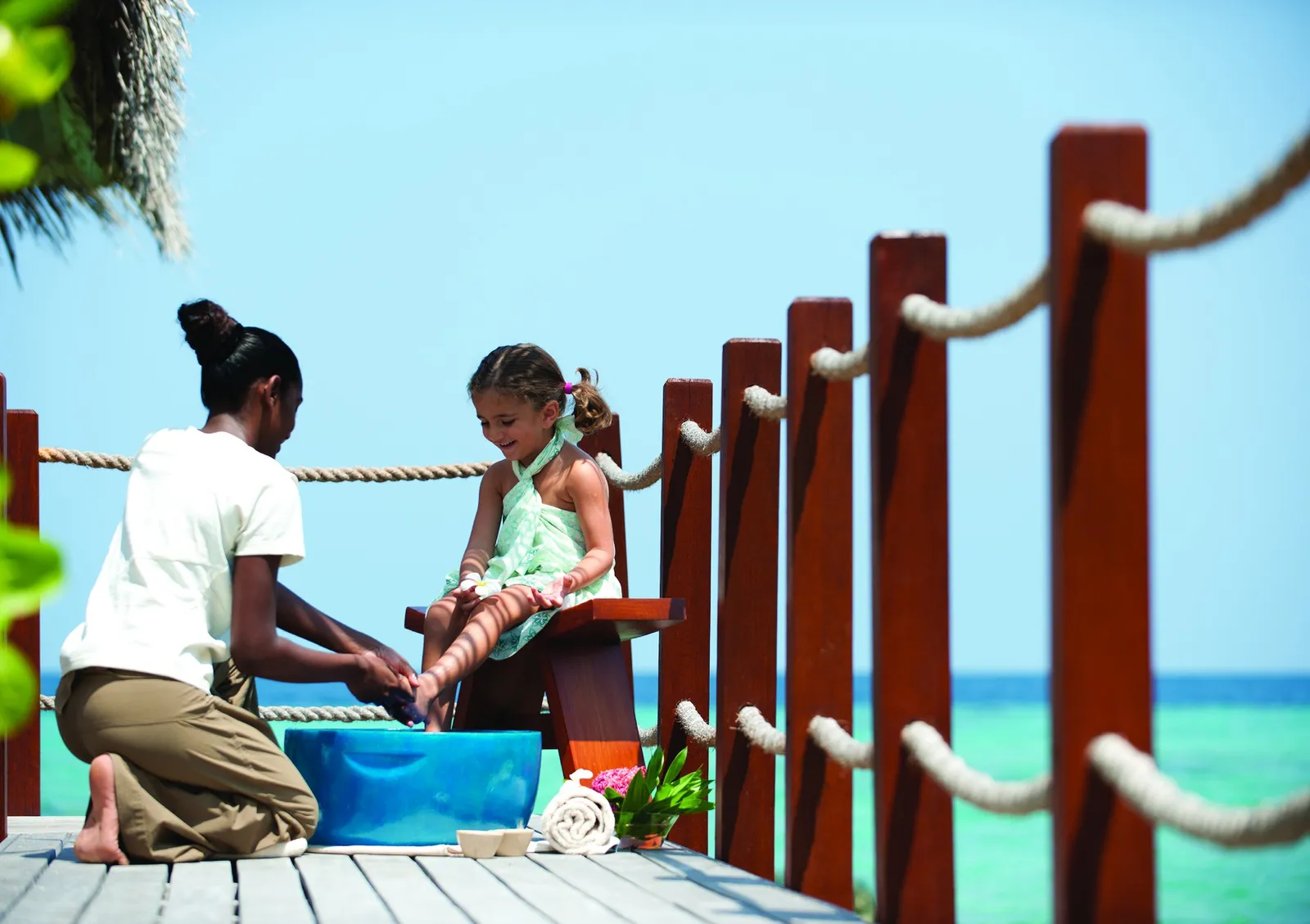 A kids’ club host playing with a little girl on a wooden jetty over the lagoon