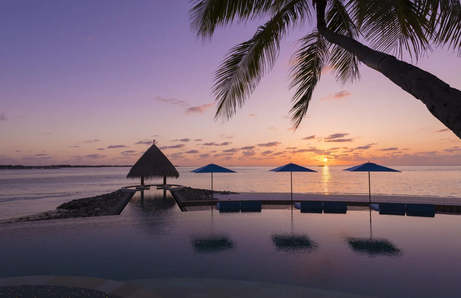 The infinity pool at sunset, with its umbrellas and the pavilion over the sea