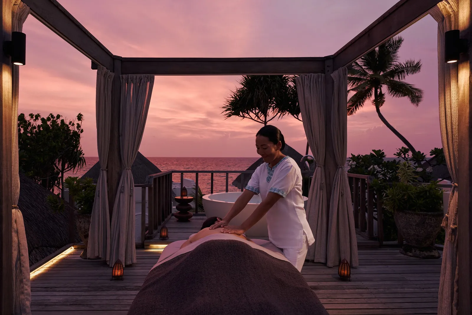 An open-air massage on the spa terrace at sunset, under a curtained gazebo