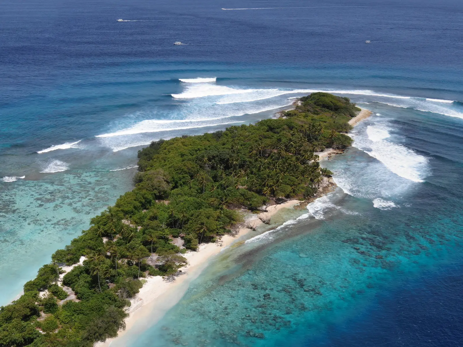 An island of the atoll from the air, with waves breaking on the outer reef