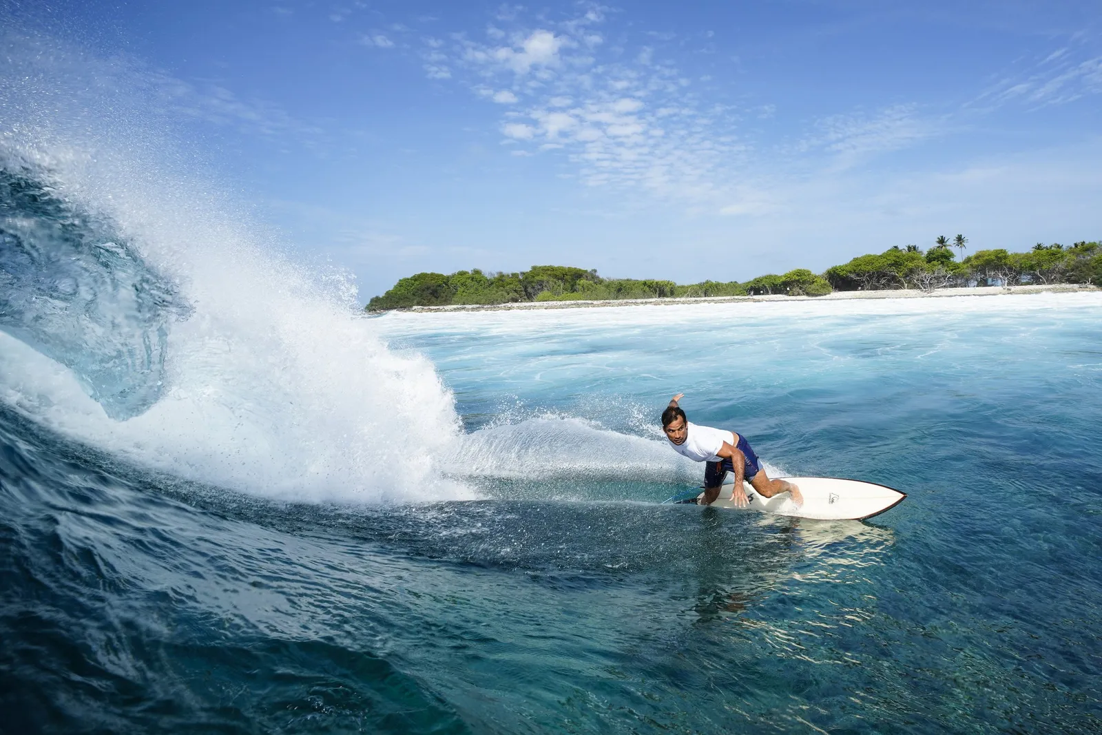 A surfer riding a wave in front of an island of the atoll