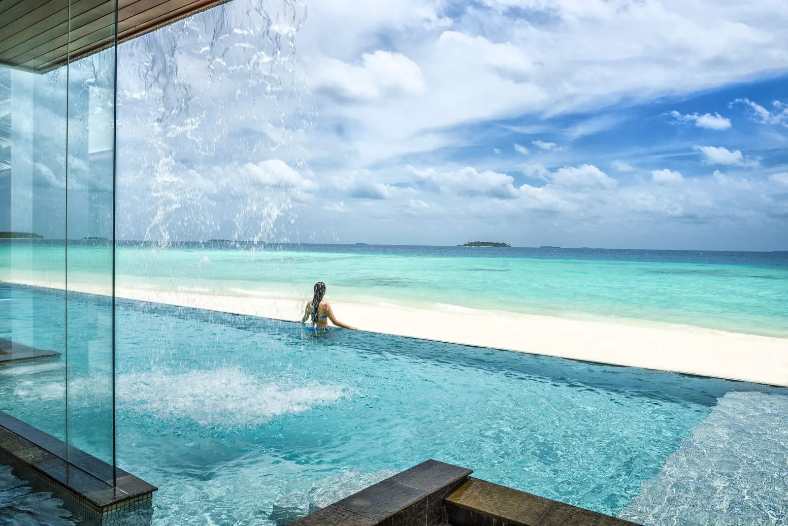 A guest in the Four-Bedroom Landaa Estate’s pool, the beach and the sea beyond its edge