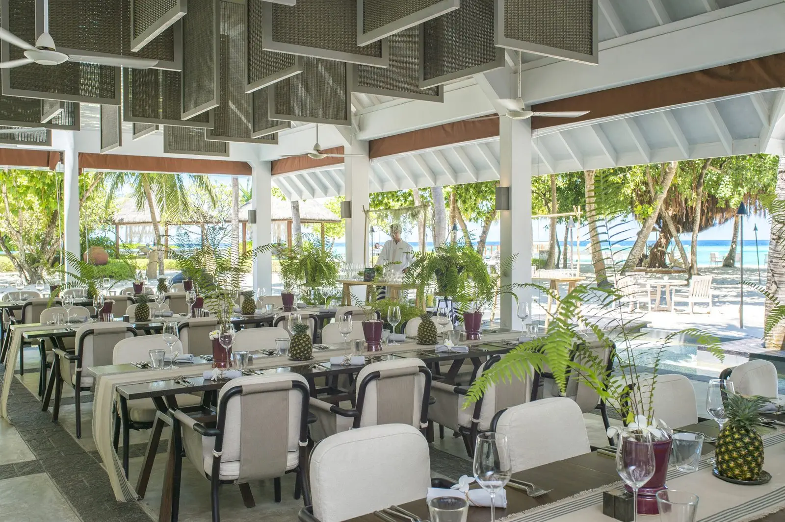 Tables in a restaurant pavilion open to the beach and the greenery