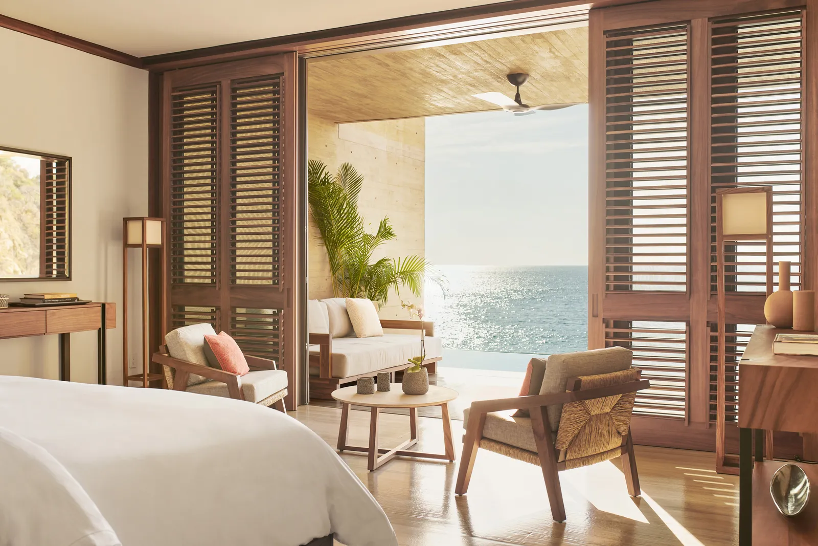 Il letto della suite Beachfront con piscina, le persiane aperte e la terrazza sul mare