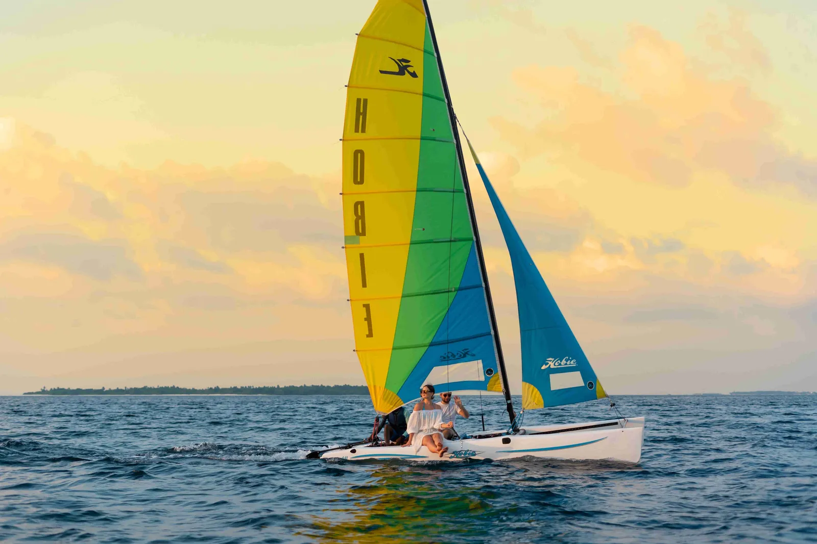 A sailing catamaran in the sunset light, 2 people aboard