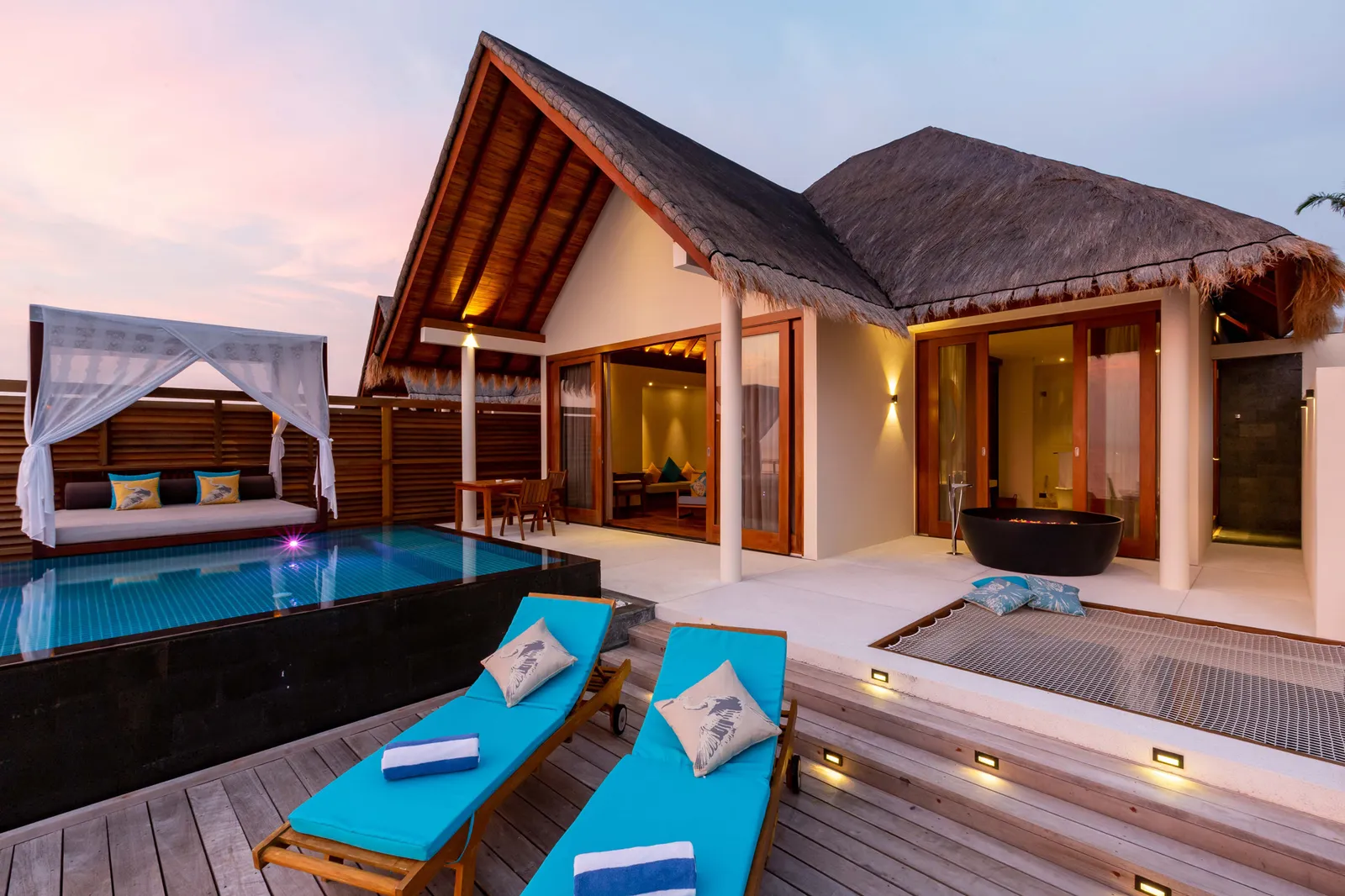 A Sunset Ocean Pool Villa at dusk, its lights on and loungers by the pool