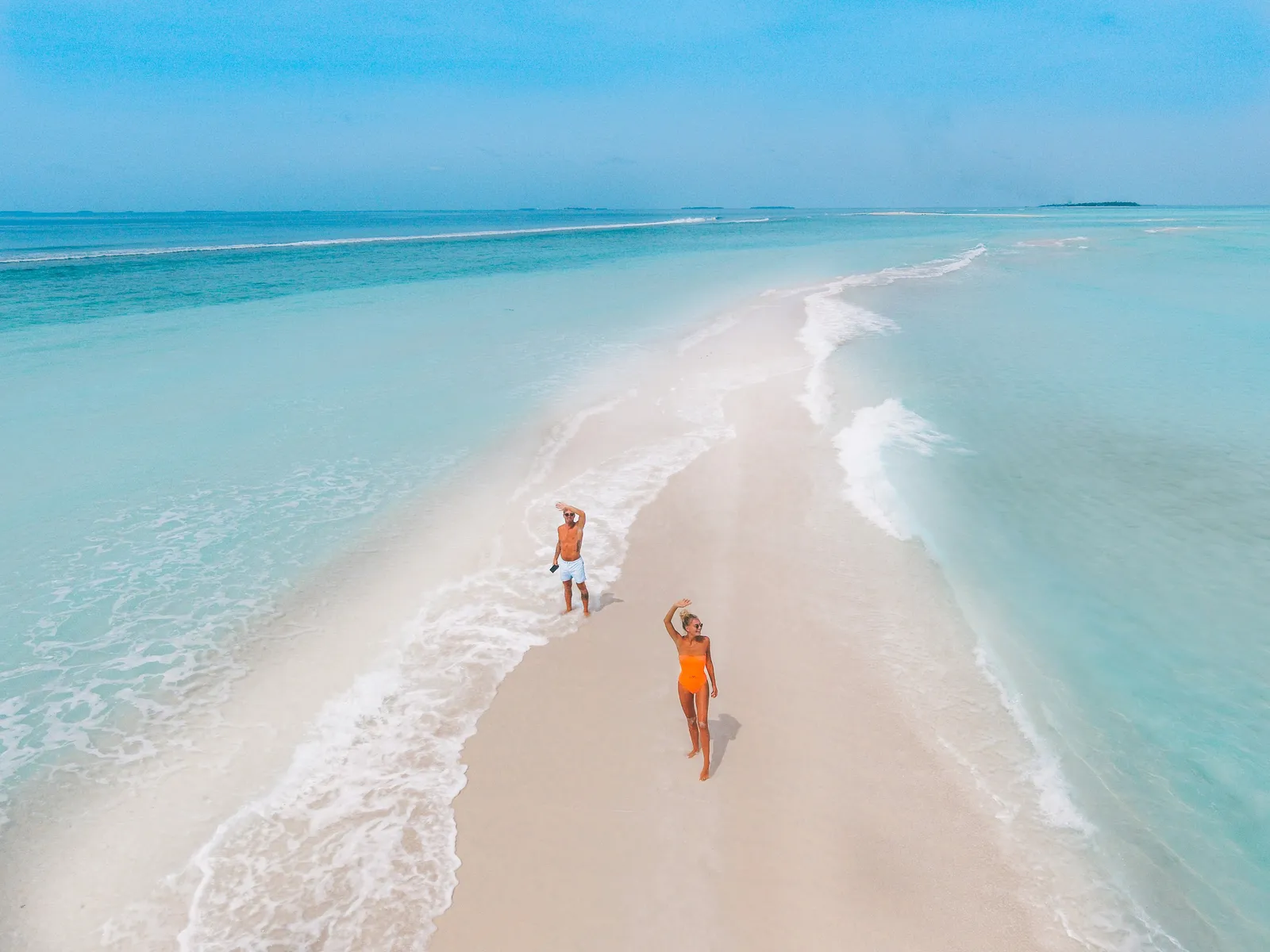 2 people on a white sandbank between 2 shades of lagoon