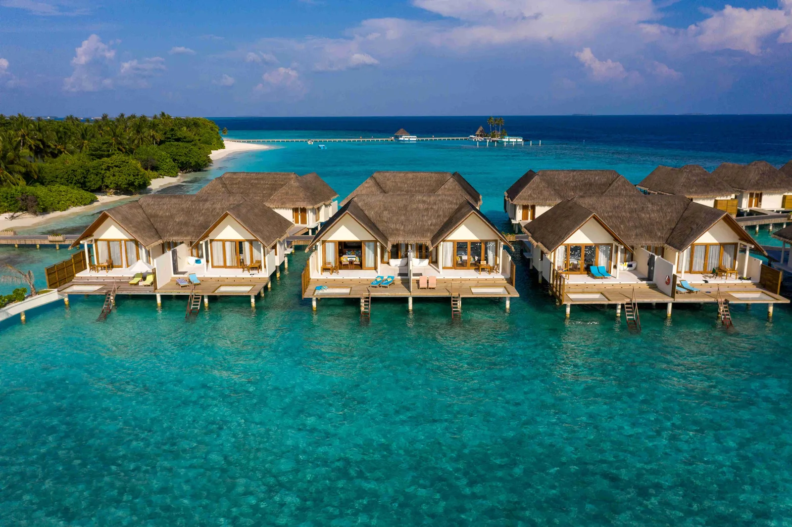 A row of water villas with ladders into the turquoise lagoon, the green island behind