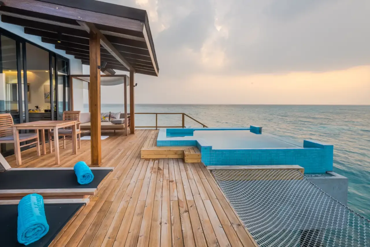 The deck of a Premium Pool Water Villa at sunset, with its pool and the net over the water.