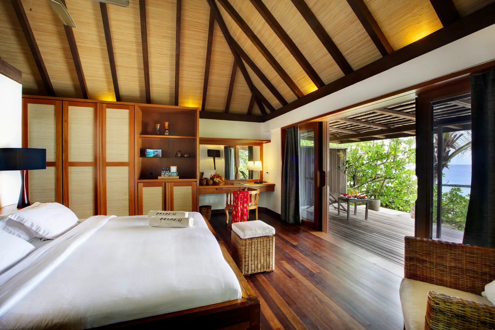 A Beach Villa bedroom under the pointed timber roof, with the bed, a desk and the door open on the veranda.