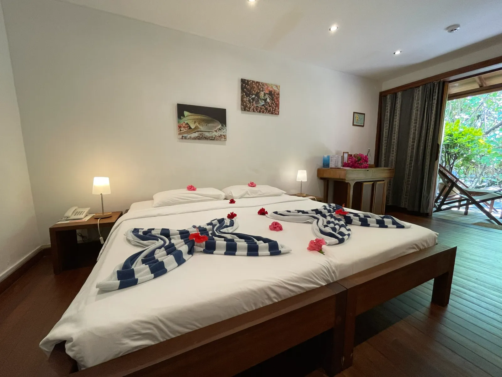 A Club Room with the bed dressed in flowers and towels, a wooden floor and the door open on the garden.