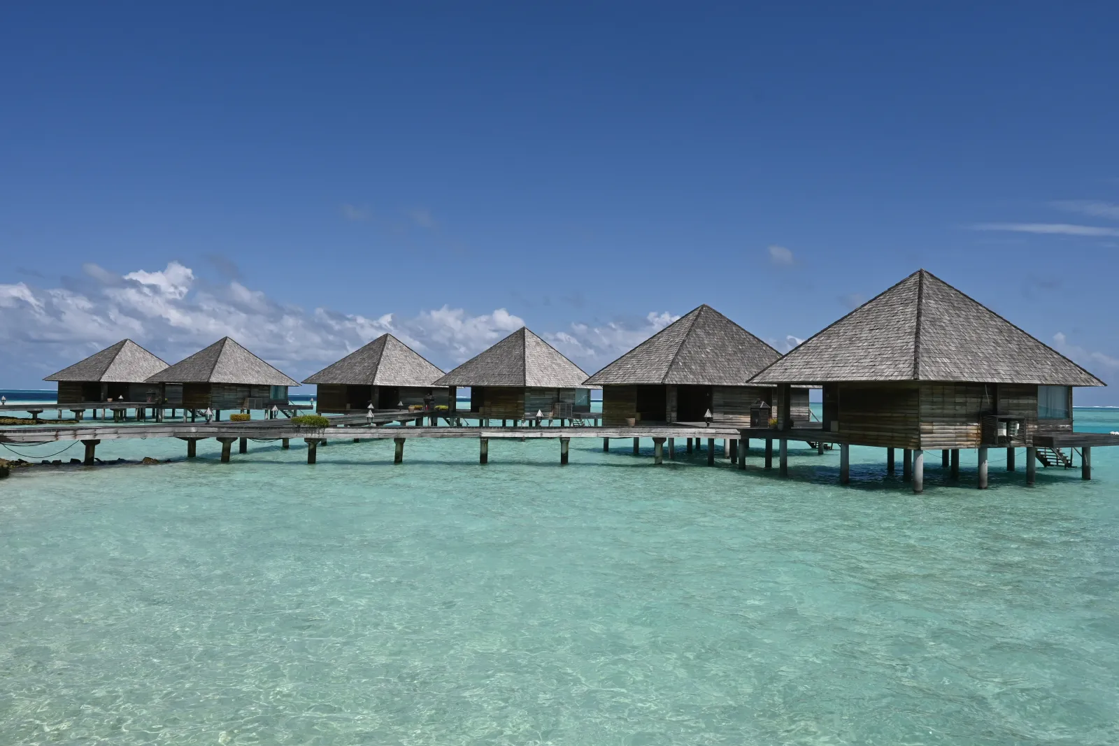 The row of Overwater Villas with their pointed roofs over the clear lagoon, joined by the jetty.