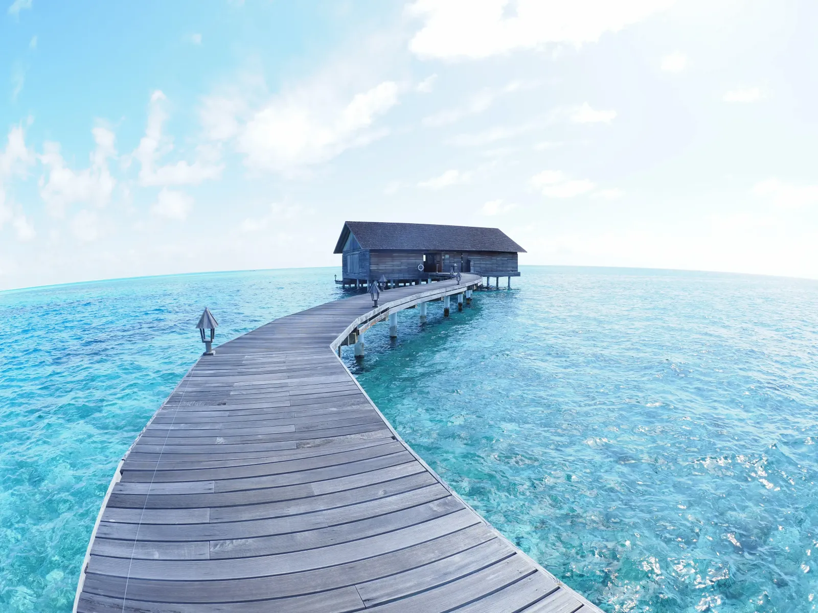 A curving wooden jetty crosses the turquoise lagoon to a pavilion on the water.
