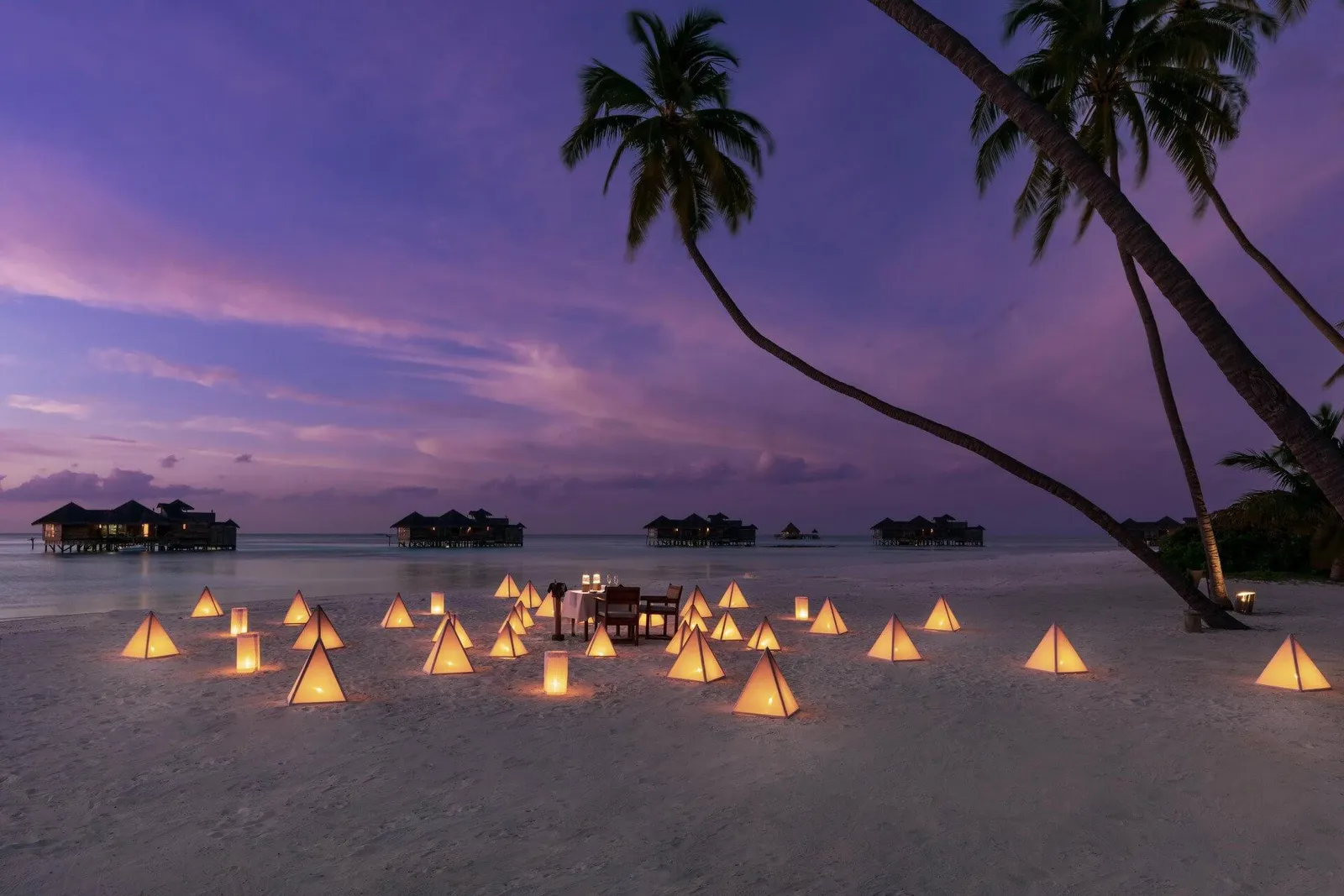 A private dinner on the beach at sunset, the table among lanterns