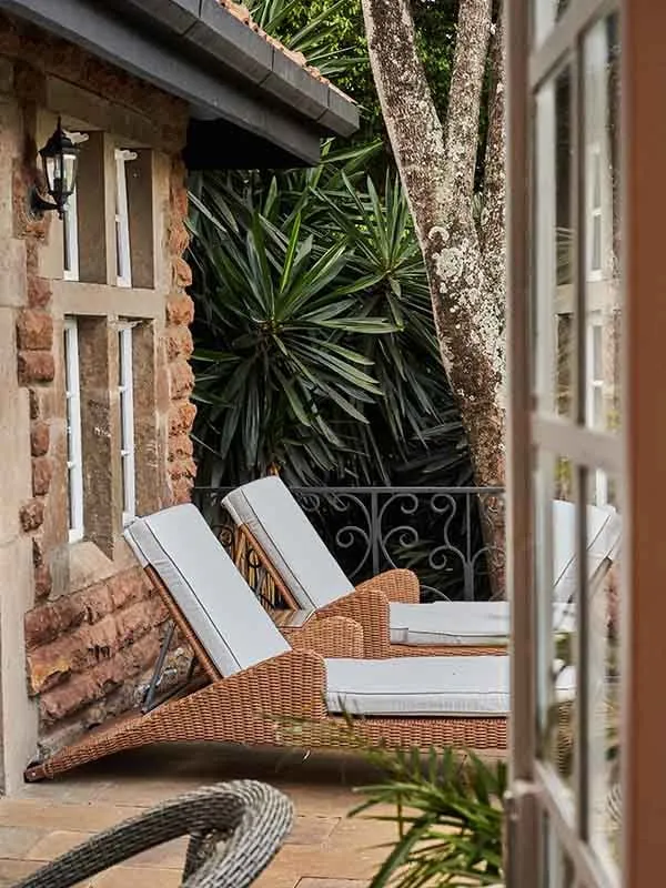 A room’s balcony, 2 white loungers and the French window open to the garden