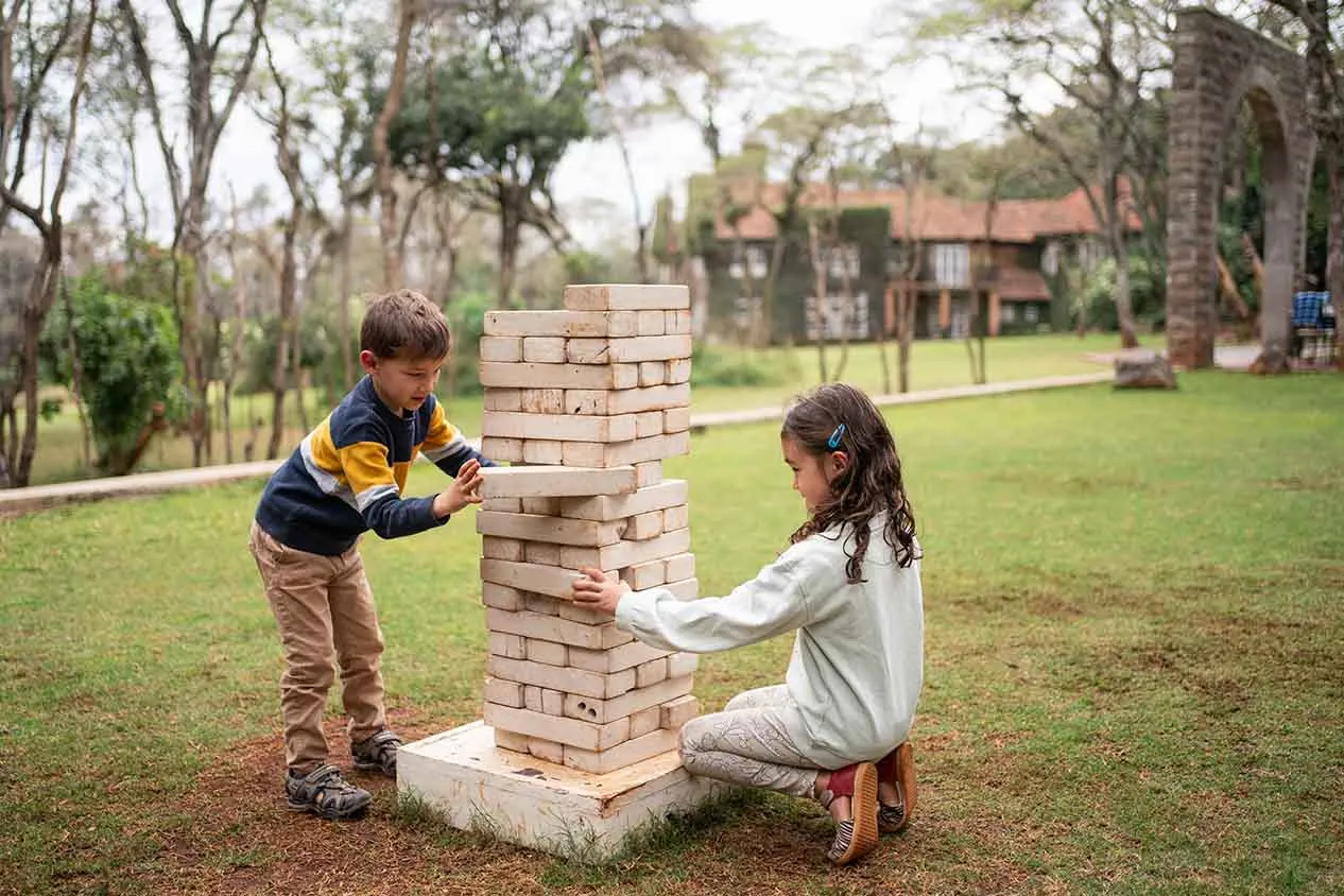 2 children play giant Jenga on the lawn, the house behind them