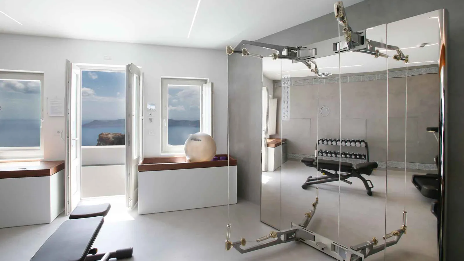The fitness studio: a bench, a steel multi-gym and 2 white French windows open to the sea.