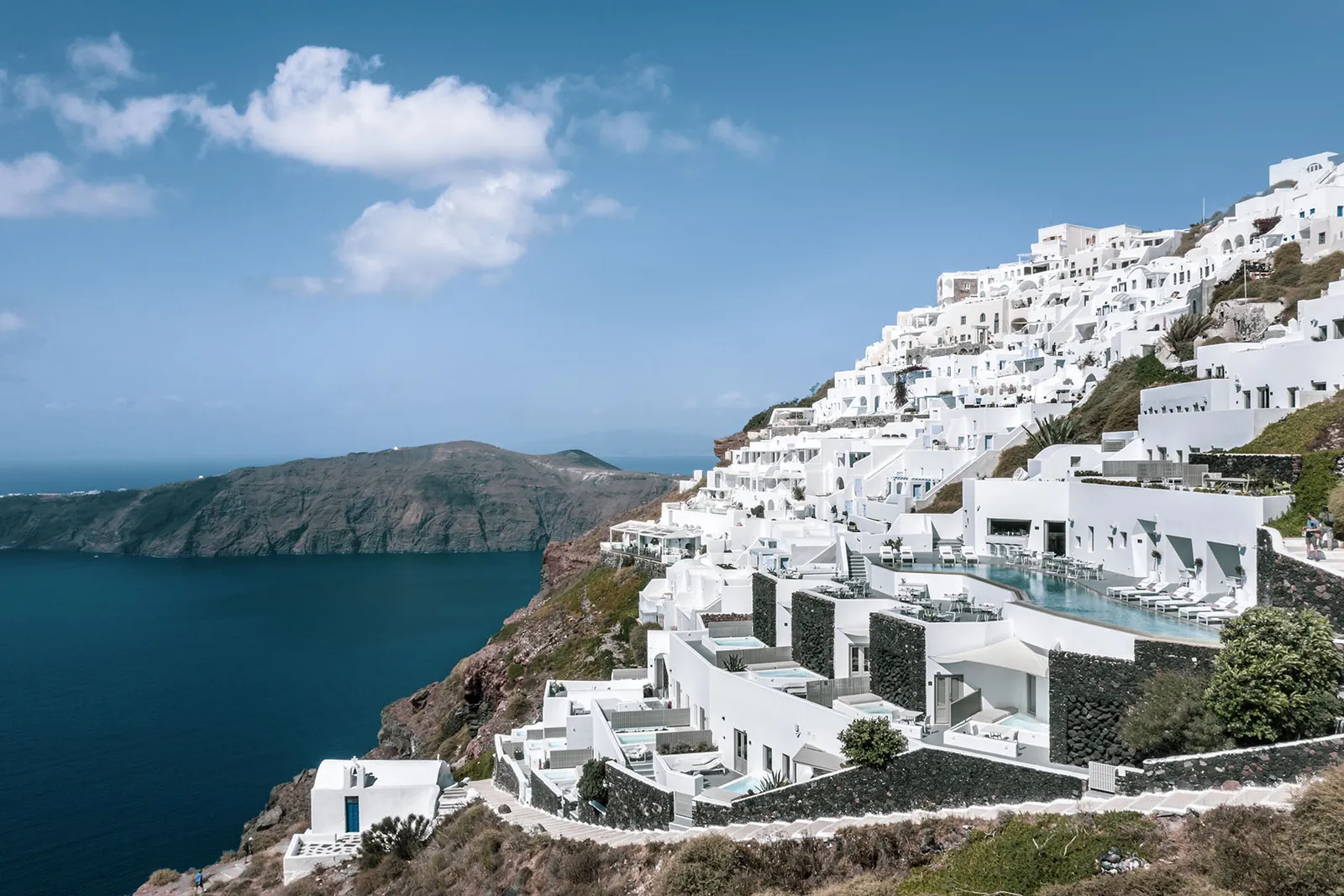 Imerovigli on its cliff in full daylight: white houses in steps, the hotel’s pool in the middle and the blue sea of the caldera.