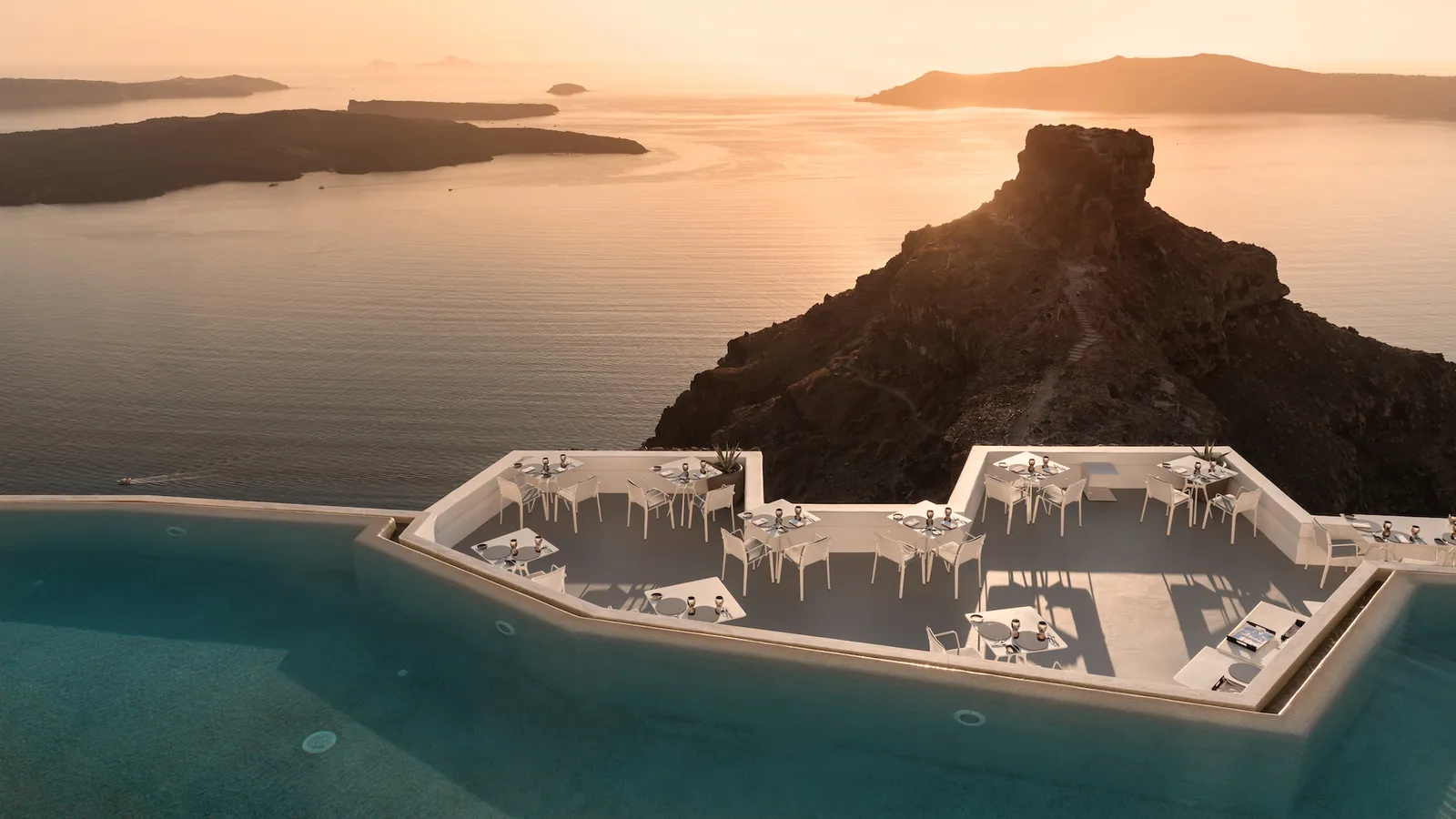 The dining platform in the pool from above at sunset, Skaros Rock in silhouette and the sea turned gold.