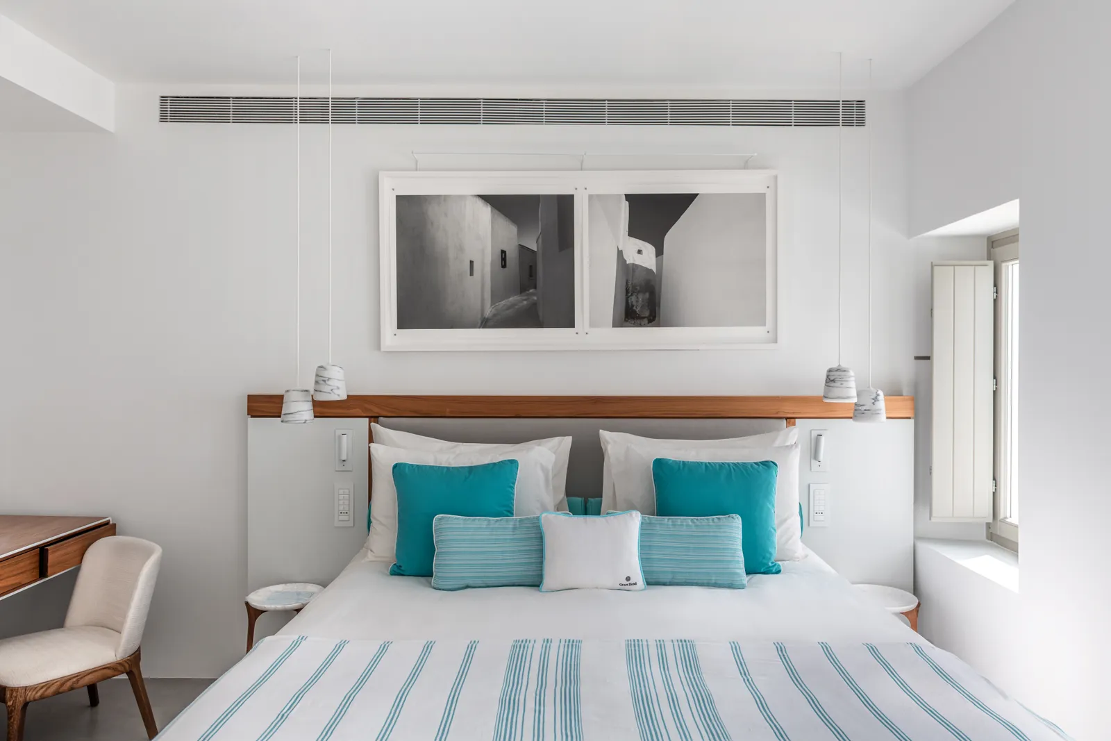 A Deluxe Room: the bed with turquoise cushions and a striped throw, 2 black-and-white photographs above the wooden headboard.