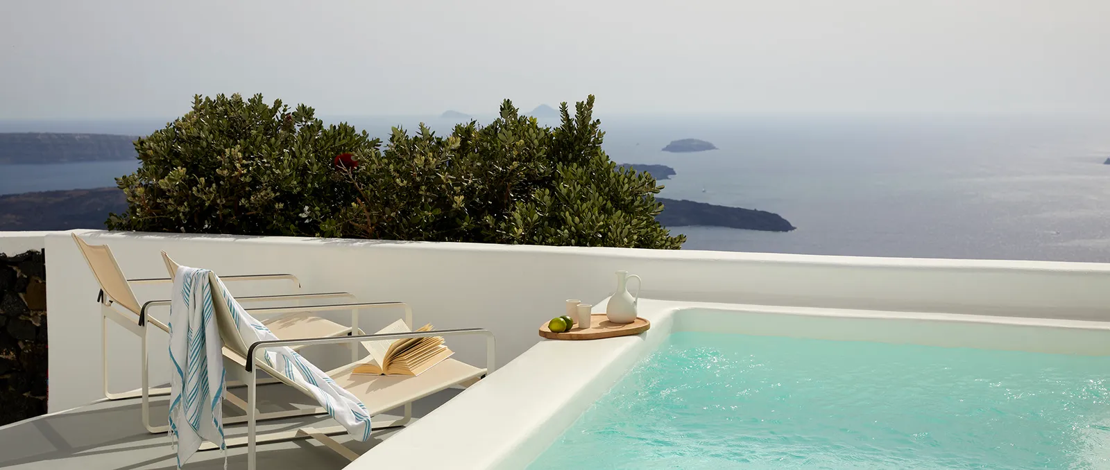 A Deluxe Room with Plunge Pool terrace: the turquoise pool, 2 deckchairs with a striped towel and the sea beyond the white wall.