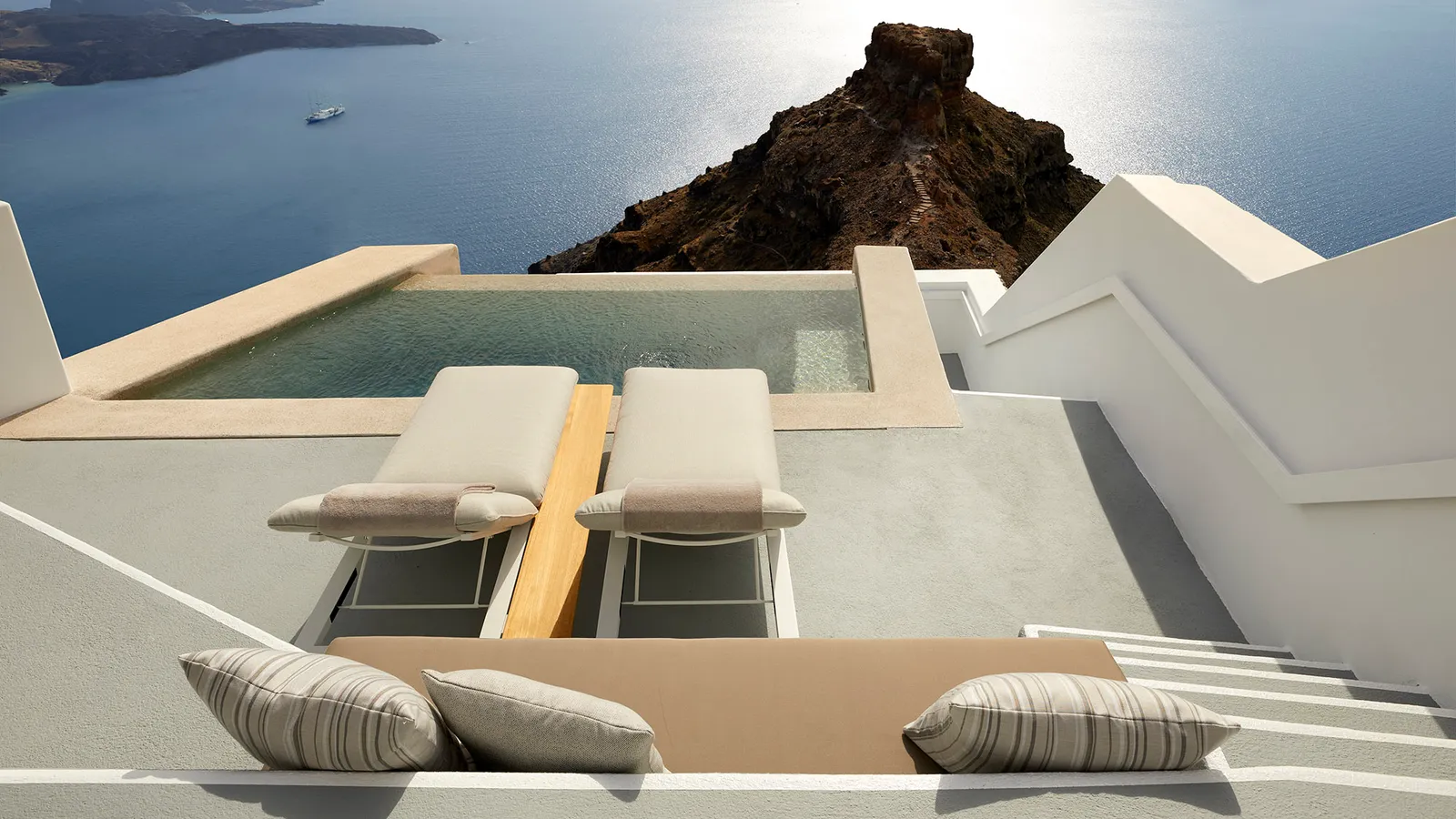 An Infinity Suite terrace: 2 loungers, striped cushions on the steps, the private pool and Skaros Rock over the sea.