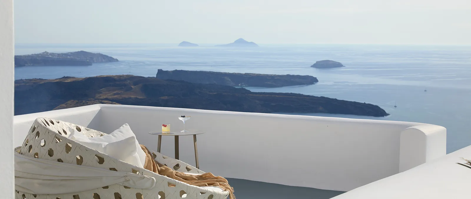 The Junior Suite’s terrace: a round white rope daybed with cushions, a side table and the caldera’s islands.