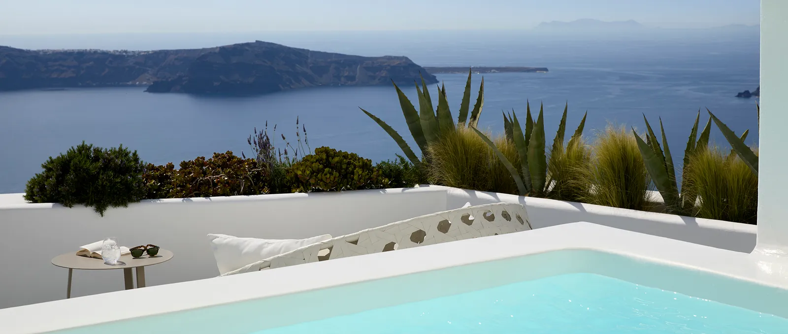 A Superior Suite’s private pool between white walls, with agaves, a side table and the caldera’s coastline.