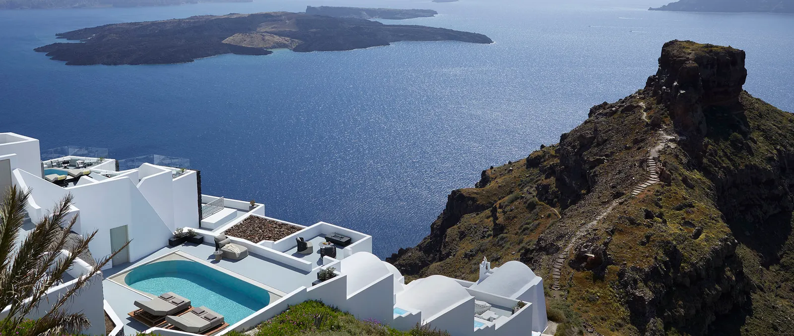 The Villa from above: its blue private pool, white terraces on several levels and the path climbing Skaros Rock.