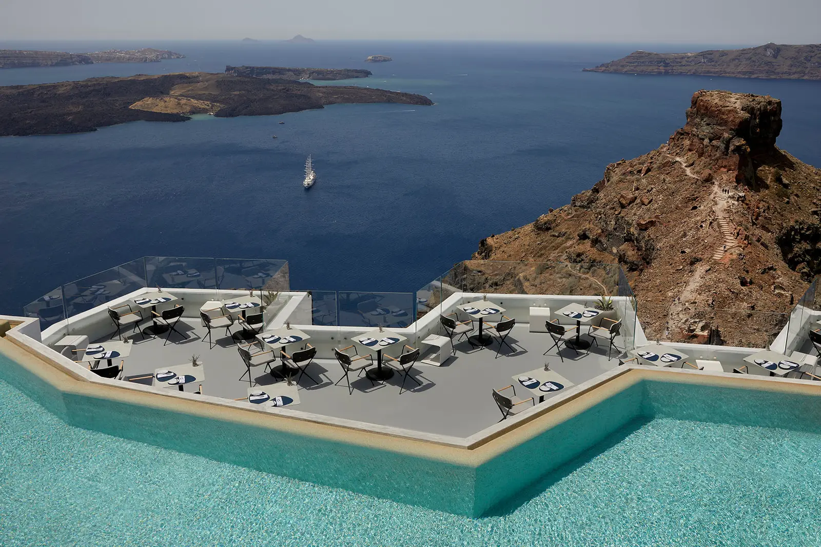 Varoulko Santorini’s tables on a platform ringed by the pool’s water, with Skaros Rock and the caldera’s islands beyond.