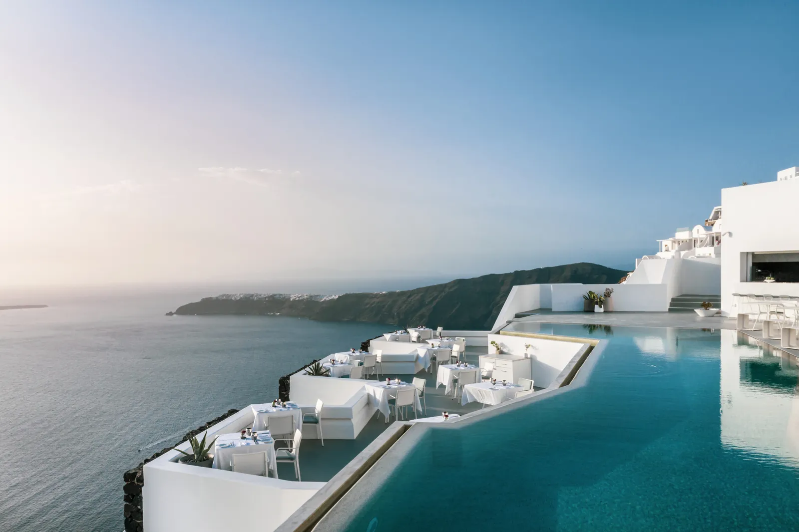 The infinity pool and the restaurant’s terraces from above, white tables laid on the cliff edge and the sea below.