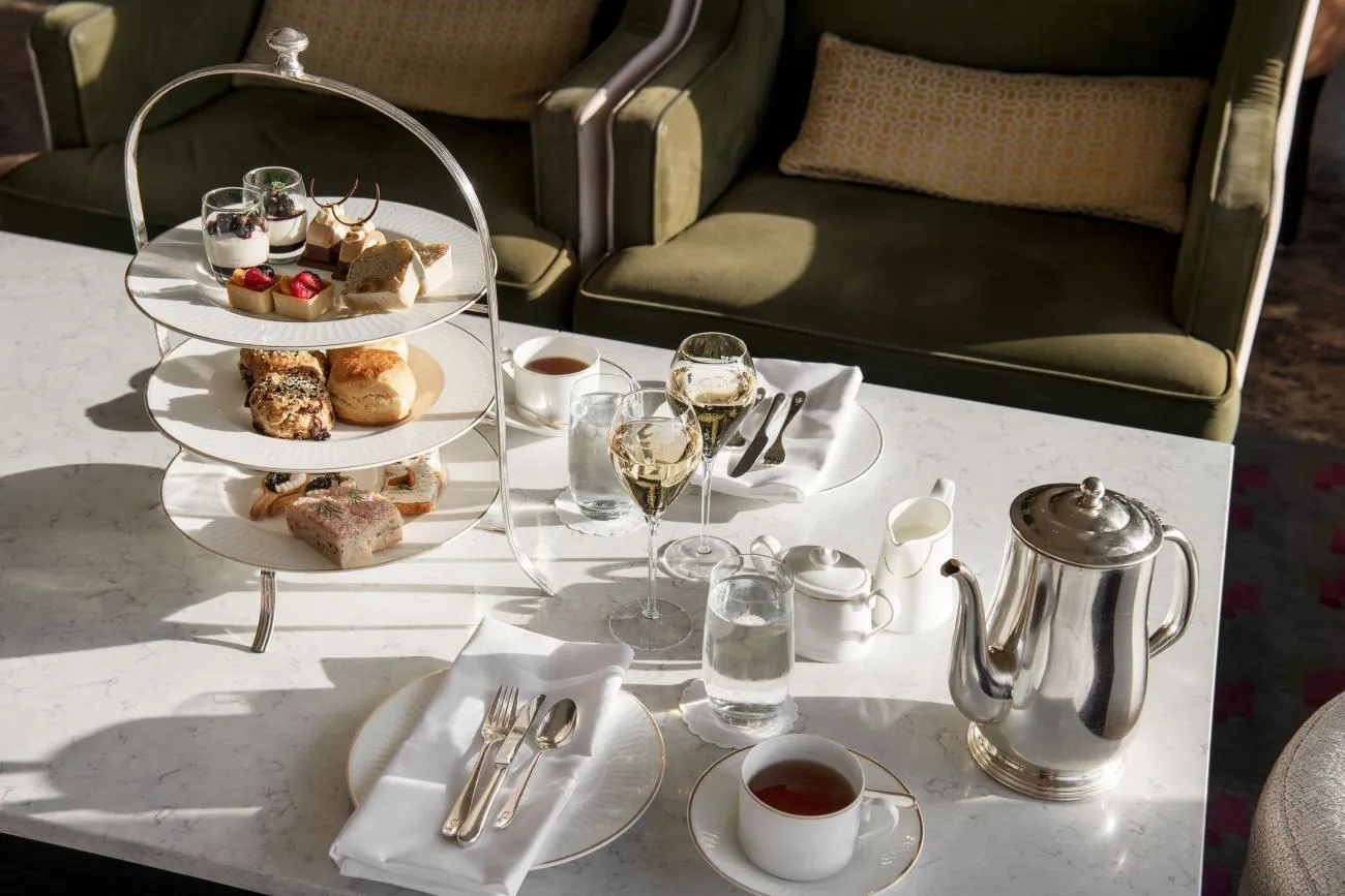 Afternoon tea in the Cadier Bar: a stand of 3 tiers with sandwiches, scones and pastries, 2 glasses of Champagne and a silver teapot on a marble table.