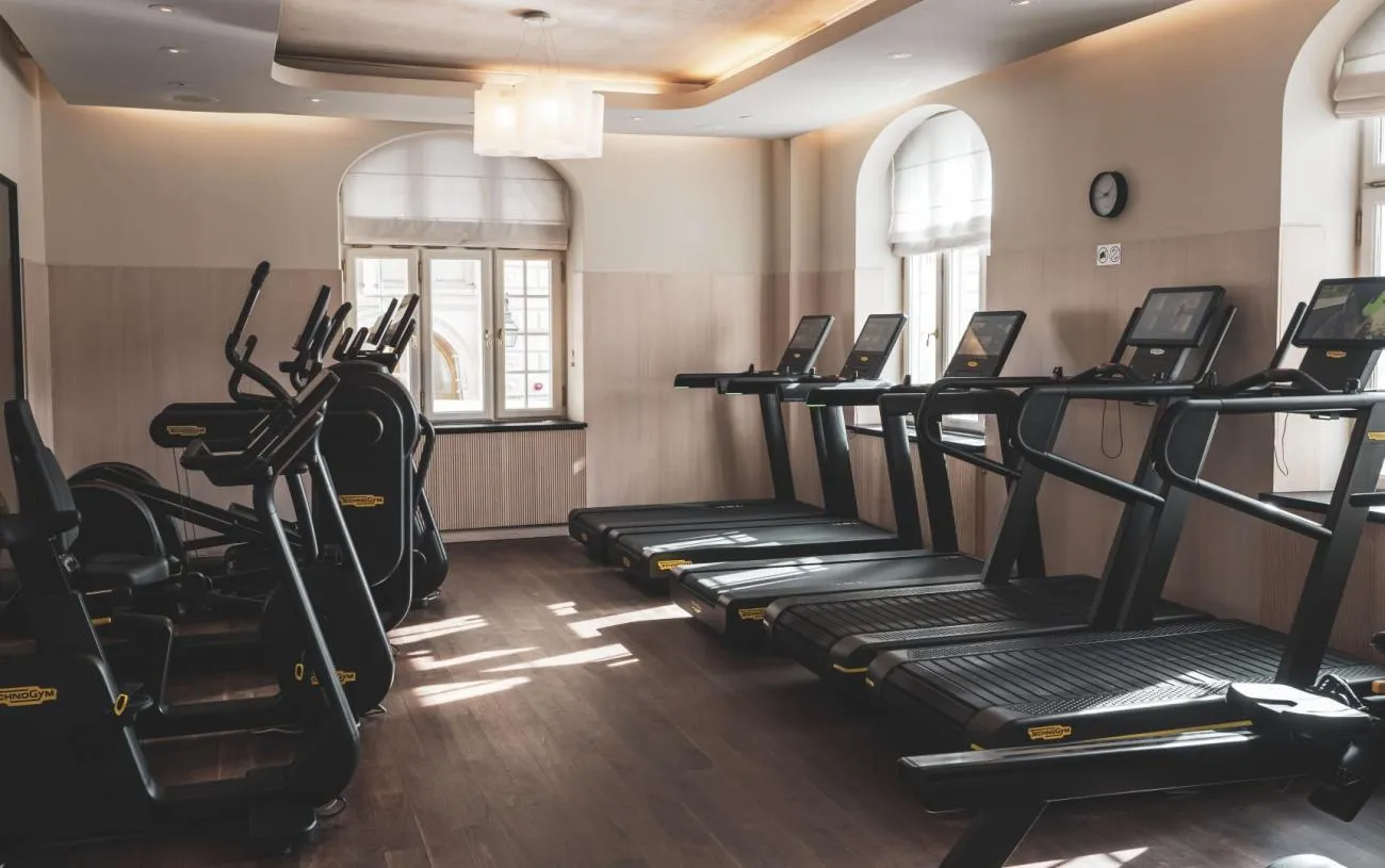 The gym: a row of treadmills and cross-trainers before arched windows, on a dark wooden floor.