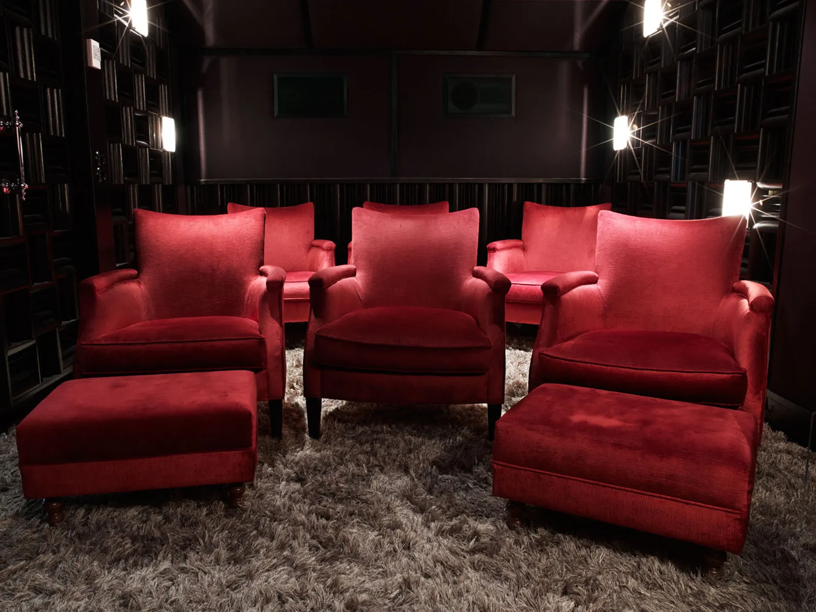 The Princess Lilian Suite’s cinema: red velvet armchairs and footstools on a deep-pile rug, in a dark-walled room.