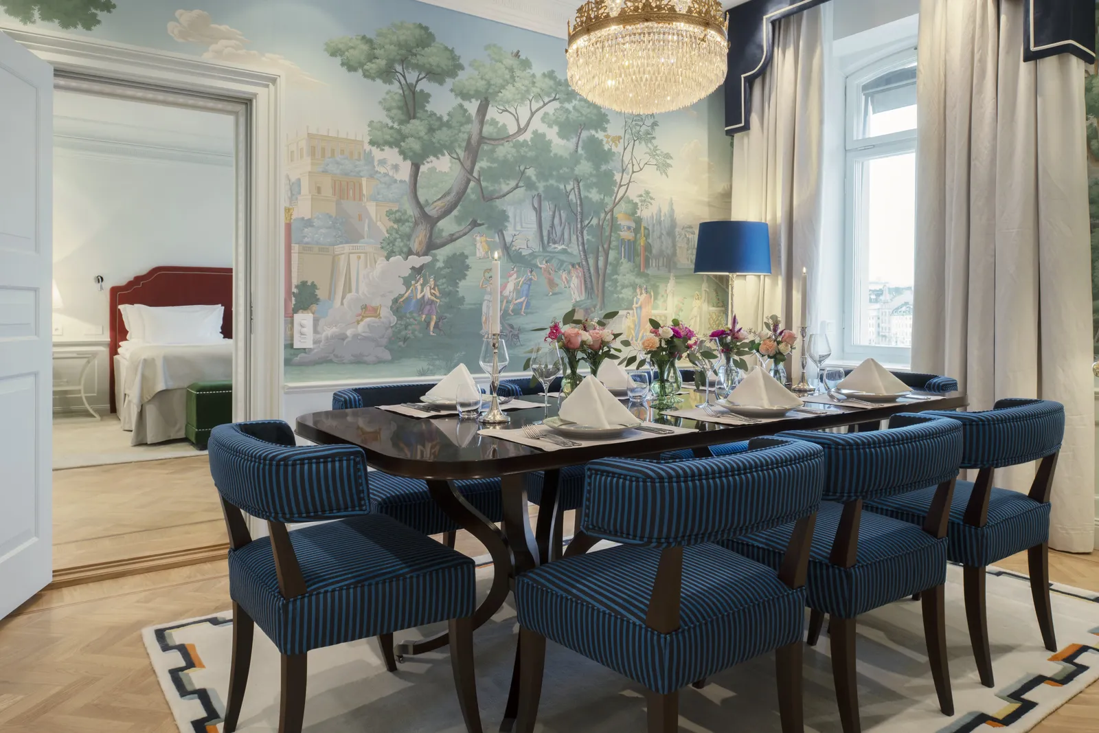 The Bernadotte Suite dining room: the table laid for 6 with blue chairs, hand-painted landscape wallpaper and the bedroom through the door.