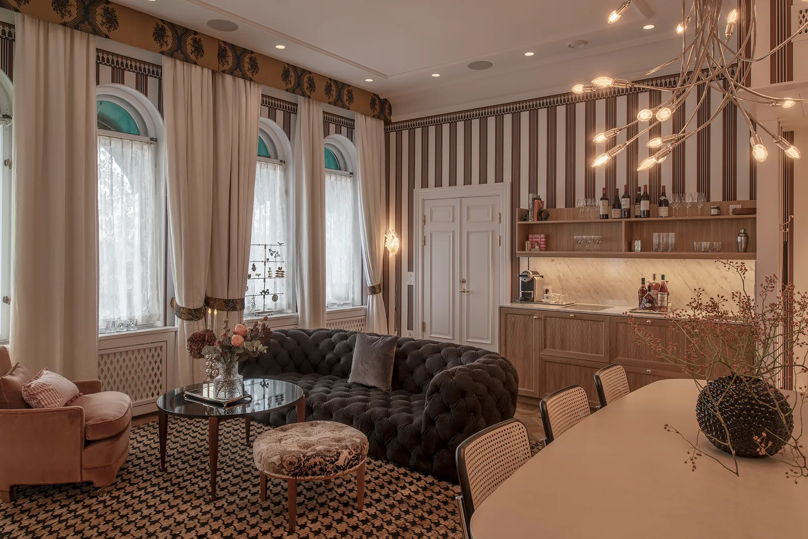 The Bolinder Suite sitting room: striped walls, a dark buttoned sofa, the pale-wood bar corner and arched windows.