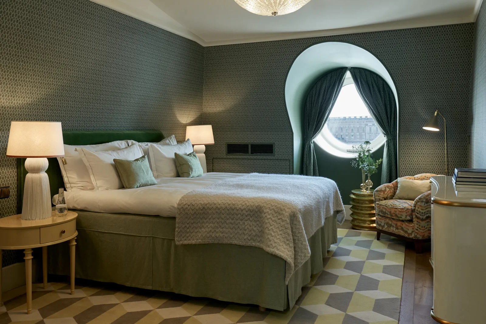 The Rooftop Suite bedroom: the king bed, dark-green wallpaper, a diamond-patterned rug and the arched window with green curtains.