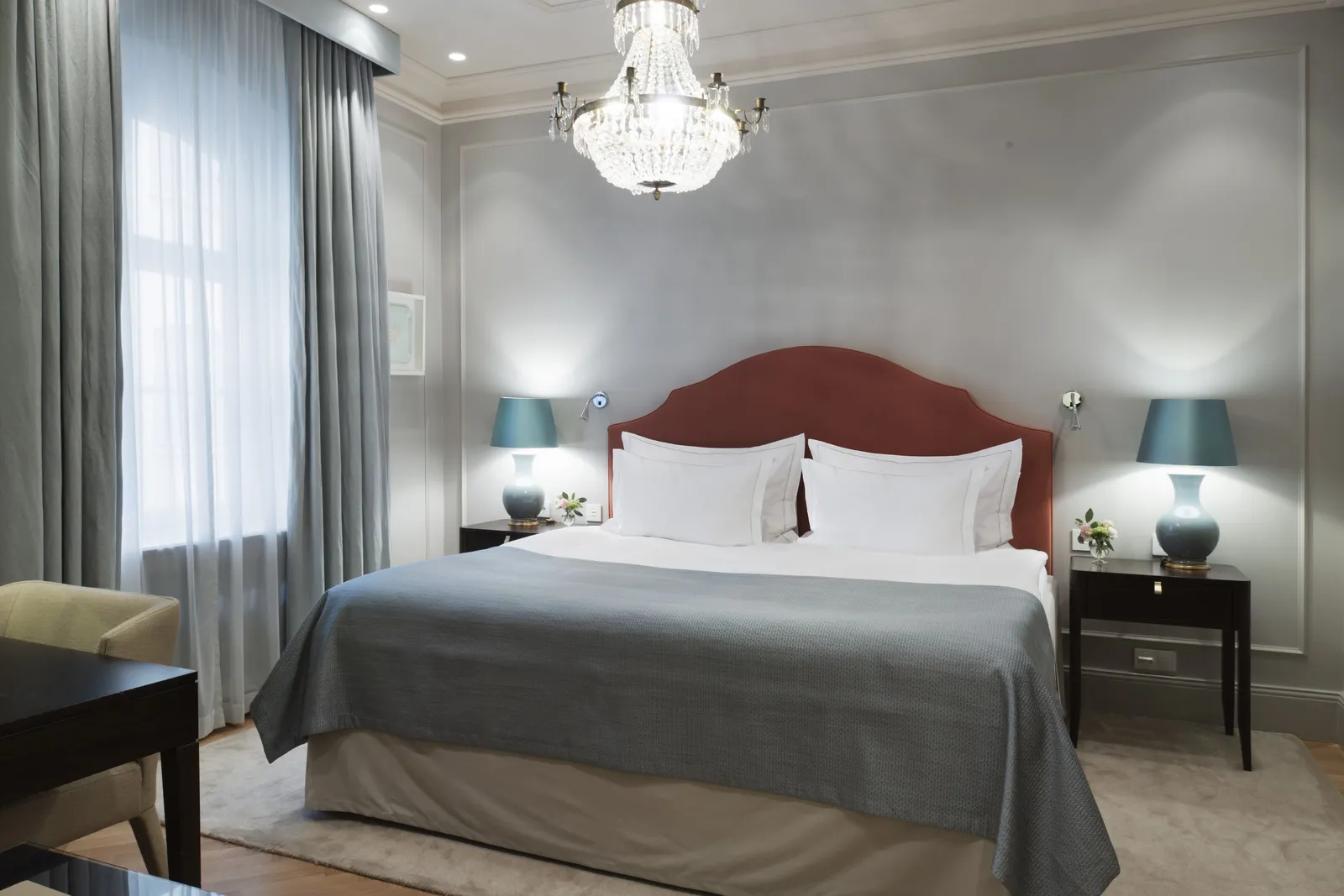 A Superior Room on the courtyard: the double bed with a brick-red headboard between 2 blue lamps, grey panelled walls and herringbone parquet.
