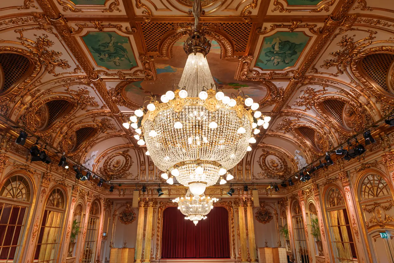 Spegelsalen: the gilded ceiling with painted coffers, the great crystal chandelier, arched mirrored doors and the red stage curtain.